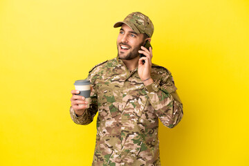 Wall Mural - Military man isolated on yellow background holding coffee to take away and a mobile