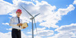 © Med Photo Studio - Young man engineer in white shirt and red safety helmet holding a tablet and verifying the wind turbine windmill.