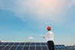 © Med Photo Studio - Young man engineer in white shirt and red safety helmet holding a tablet and verifying the photovoltaic panels at the solar power plant.