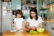 © Maria - Mother and little daughter sitting in the kitchen, making vegetable salad, drawing. Happy family concept. Daily home life