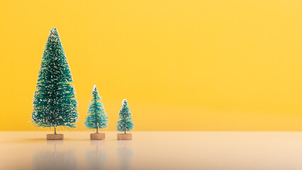 miniature green Christmas tree sits on white table and has bright yellow background that contrasts nicely with green Christmas tree and has a copy space to insert text to create greeting card.