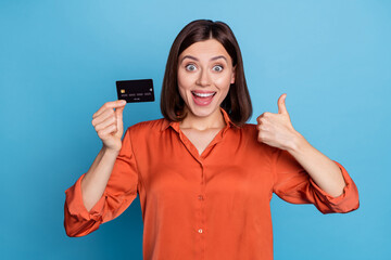 Poster - Portrait of attractive trendy cheerful girl holding in hand bank card showing thumbup isolated over bright blue color background