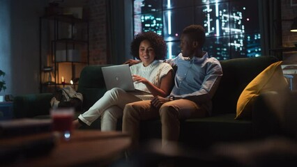Poster - Young Black Couple Use Laptop Computer, while Sitting on a Couch in Cozy Stylish Apartment. Boyfriend and Girlfriend do Online Shopping, Use Social Media, Watch Funny Videos, Streaming Service