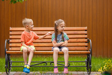 Boy And Girl Sitting On A Bench. On A Sunny Summer Day, A Five-year-old Boy And A Girl Are Sitting On A Bench In The Garden.