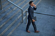 © Mediaphotos - Positive young black lawyer in stylish suit moving down stairs and talking by phone while leaving court