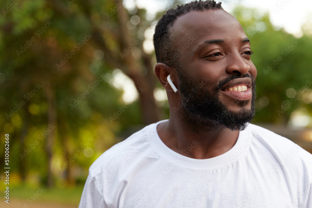 Smiling young adult african american man walking in the park wearing headphones