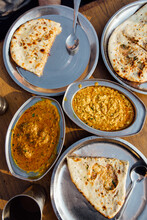 Two Bowls Of Indian Curry Dishes And Lots Of Naan