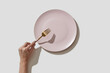 © Yaroslav Danylchenko/Stocksy - Woman holding golden fork near empty pink plate