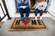 © Maria Manco/Stocksy - Children sitting on front porch of home with welcome mat