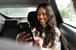© McKinsey Jordan/Stocksy - Woman In Backseat Of Car Smiles At Smartphone