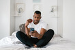 © Ezequiel Giménez/Stocksy - Black guy using smartphone and eating apple on bed