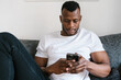 © Ezequiel Giménez/Stocksy - African American man using cellphone on couch