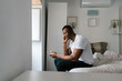 © Ezequiel Giménez/Stocksy - Smiling black male chatting on smartphone on bed