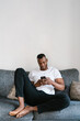 © Ezequiel Giménez/Stocksy - Glad black man browsing social media on sofa