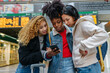 © VICTOR TORRES/Stocksy - Cheerful multiethnic friends browsing smartphone in train station
