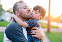 Boy Hugs And Kisses Father At Sunset