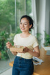 © Marc Tran/Stocksy - Smiling businesswoman eating healthy food at work and having breakfast