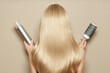 Back view of woman with long beautiful blond hair isolated on beige background holds hairdressing accessories. Dyeing and hair care. Shiny smooth blonde hair