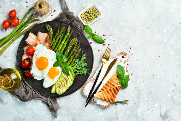 Breakfast. Scrambled eggs, asparagus, bacon and avocado. On a black stone plate.