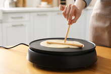 Woman Cooking Delicious Crepe On Electrical Pancake Maker In Kitchen, Closeup