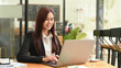 © Prathankarnpap - Smiling asian woman in business suit using laptop computer at coffee shop
