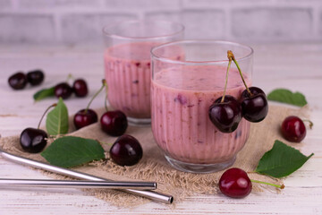 Two glasses of cherry and banana smoothie on a white wooden background.
