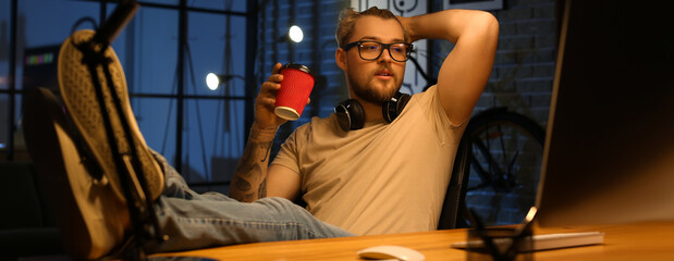 Canvas Print - Young man drinking coffee while working at home late in evening