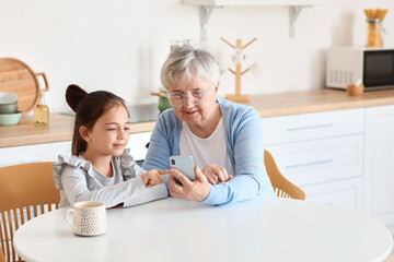 Poster - Little girl with her grandma using mobile phone in kitchen