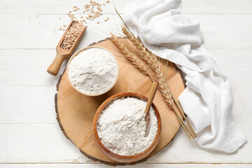 Wall Mural - Bowls with wheat flour on board against white wooden background