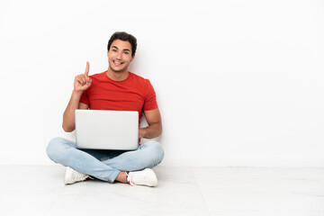 Wall Mural - Caucasian handsome man with a laptop sitting on the floor showing and lifting a finger in sign of the best