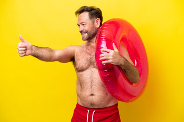 Wall Mural - Middle age caucasian man holding inflatable donut isolated on yellow background giving a thumbs up gesture