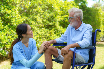 Asian nurse sitting on a hospital bed next to an older man helping hands care in garden at home. Elderly patient care and health lifestyle, medical concept.