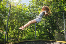 Preteen Girl Having Fun Bouncing On A Trampoline In A Backyard On A Summer Day