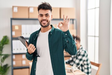 Wall Mural - Two hispanic men working at small business ecommerce doing ok sign with fingers, smiling friendly gesturing excellent symbol