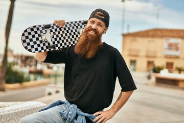 Wall Mural - Young irish skater man smiling happy holding skate at the city.