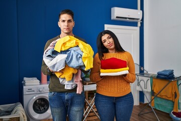 Sticker - Young couple holding laundry dirty and clean laundry relaxed with serious expression on face. simple and natural looking at the camera.