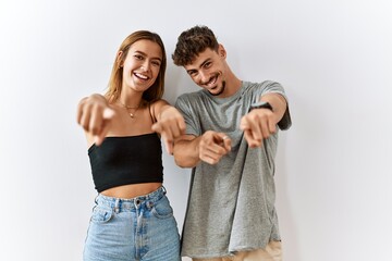 Wall Mural - Young beautiful couple standing together over isolated background pointing to you and the camera with fingers, smiling positive and cheerful