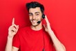 © Krakenimages.com - Young hispanic man wearing call center agent headset surprised with an idea or question pointing finger with happy face, number one