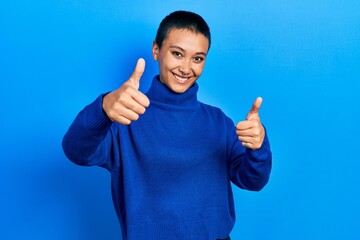 Poster - Beautiful hispanic woman with short hair wearing turtleneck sweater approving doing positive gesture with hand, thumbs up smiling and happy for success. winner gesture.