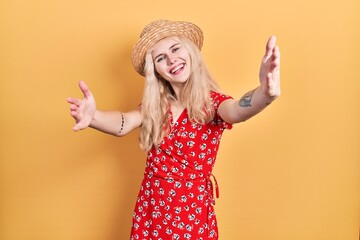 Sticker - Beautiful caucasian woman with blond hair wearing summer hat looking at the camera smiling with open arms for hug. cheerful expression embracing happiness.