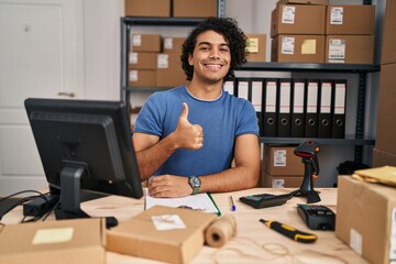 Canvas Print - Hispanic man with curly hair working at small business ecommerce doing happy thumbs up gesture with hand. approving expression looking at the camera showing success.