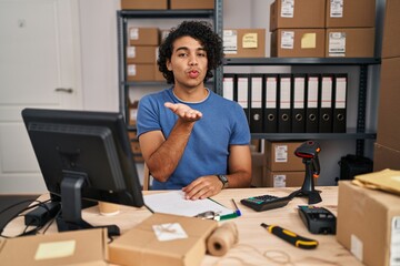 Poster - Hispanic man with curly hair working at small business ecommerce looking at the camera blowing a kiss with hand on air being lovely and sexy. love expression.