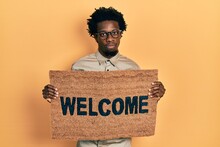 Young African American Man Holding Welcome Doormat Skeptic And Nervous, Frowning Upset Because Of Problem. Negative Person.