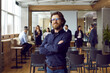 canvas print picture Portrait of business teacher and team coach. Happy handsome bearded young man in blue shirt and eyeglasses standing in office after corporate training class, with group of employees in background