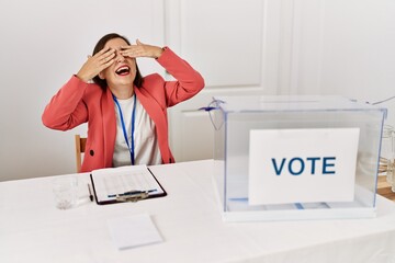 Poster - Beautiful middle age hispanic woman at political election sitting by ballot covering eyes with hands smiling cheerful and funny. blind concept.