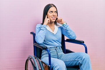 Poster - Beautiful woman with blue eyes sitting on wheelchair covering ears with fingers with annoyed expression for the noise of loud music. deaf concept.