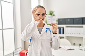 Wall Mural - Young doctor woman holding covid certificate smiling happy doing ok sign with hand on eye looking through fingers