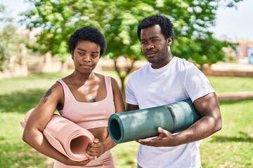 Poster - African american man and woman couple holding yoga mat with relaxed expression at park