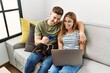 © Krakenimages.com - Young hispanic couple smiling happy using laptop and credit card sitting on the sofa  with dog at home.