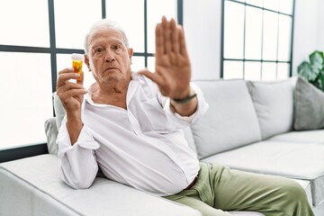 Poster - Senior man holding pills doing stop sing with palm of the hand. warning expression with negative and serious gesture on the face.